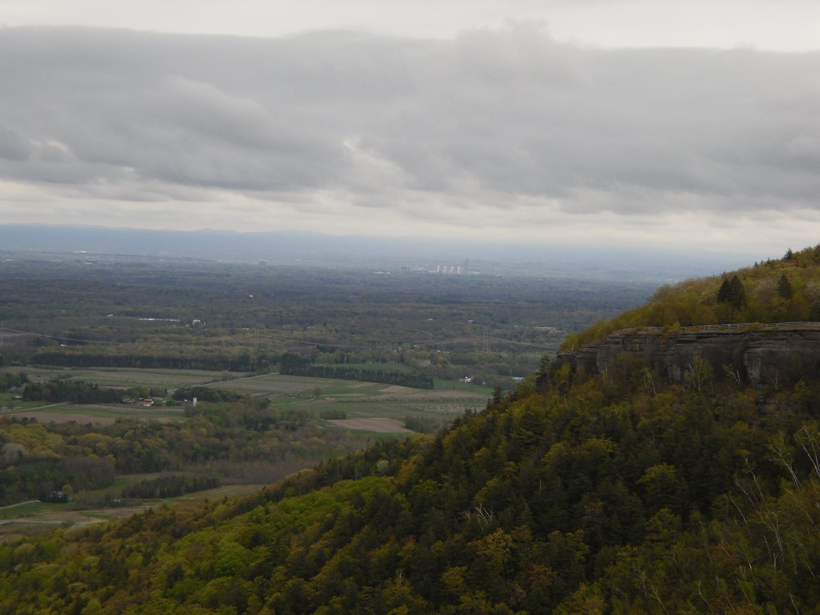 Farm fields, hedgerows and woodland spread across the valley below the Helderberg cliff line under a heavy sky.